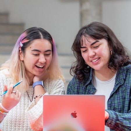 Two tertiary students looking at a laptop and smiling
